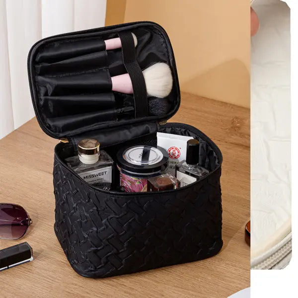 Black quilted makeup bag with cosmetic items on a wooden surface