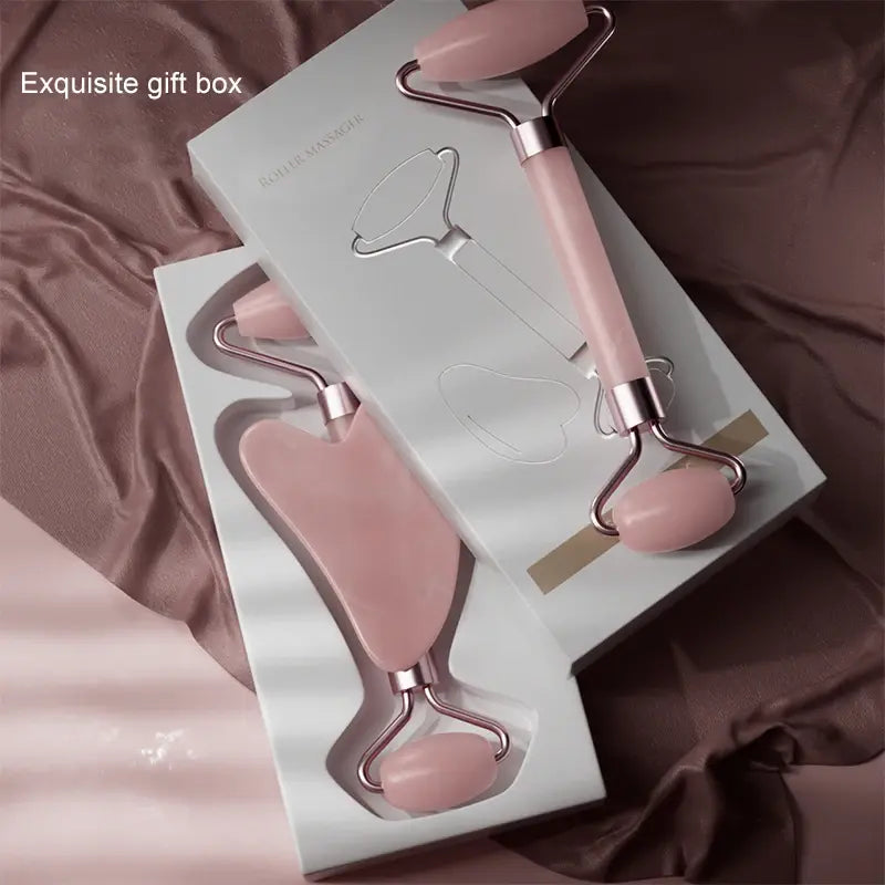 Pink facial roller and massage tool set in an open box on a brown fabric background